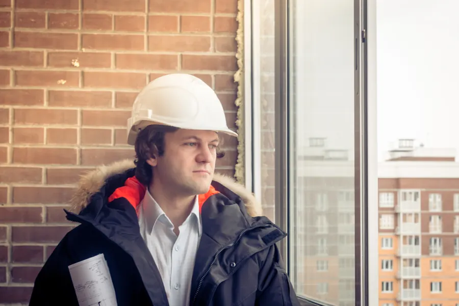 Architect in a hard hat holding plans beside a window